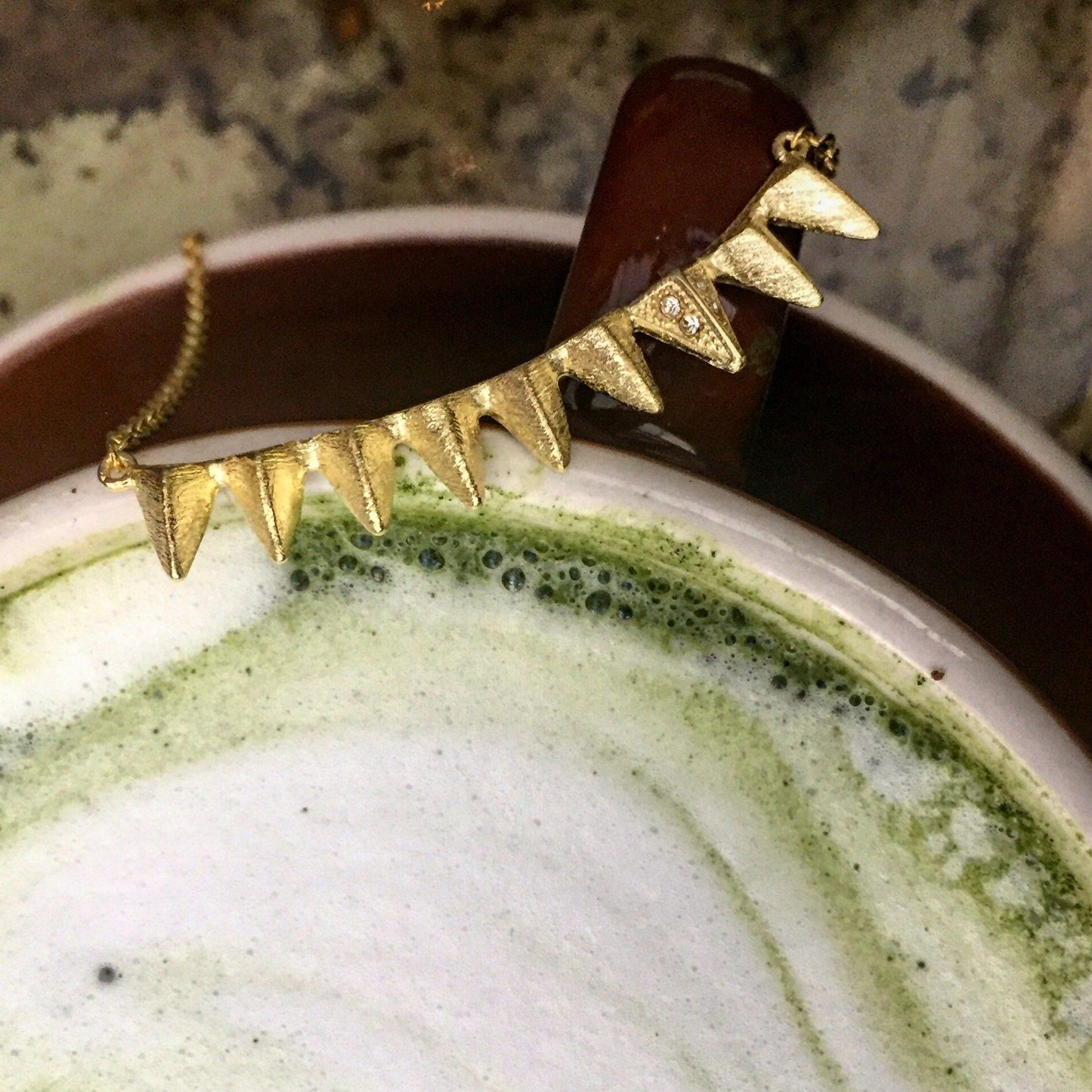 Mantra Multi Triangle Necklace with Swarovski crystals on a brown cup of matcha latte