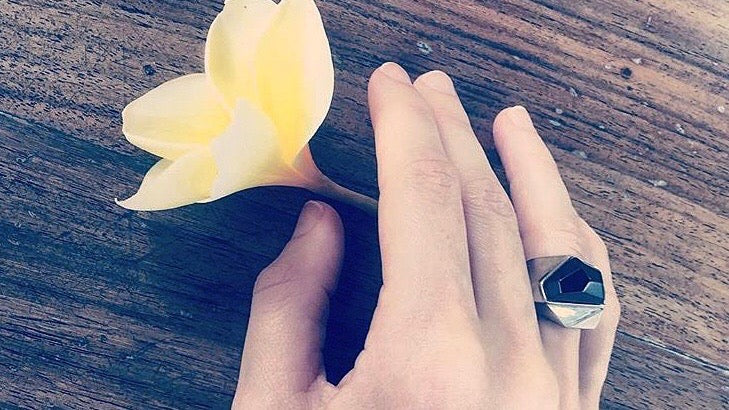 hand on table next to yellow flower wearing Lattice Cocktail Ring in Black Agate