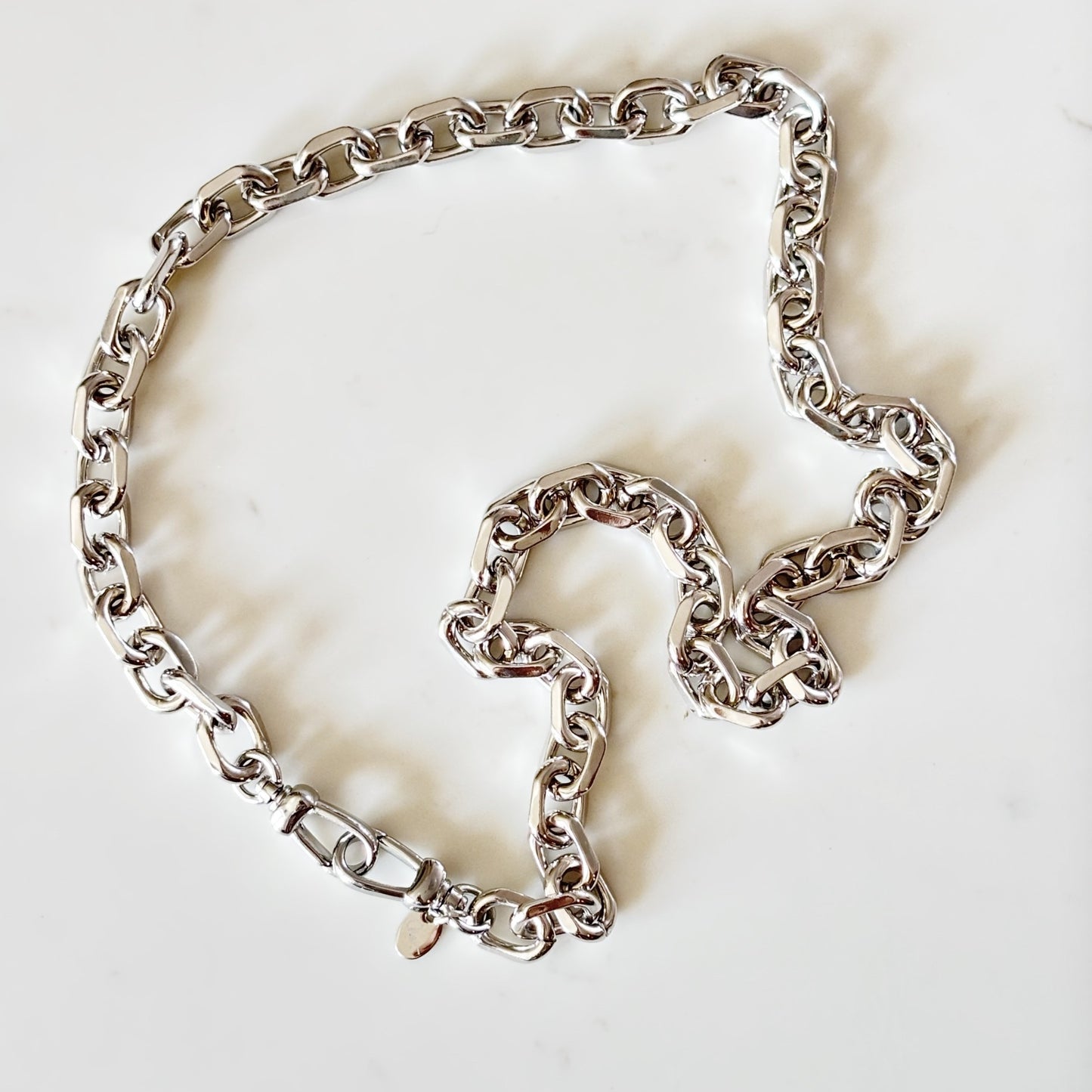 Riley - silver-toned metal chain necklace with a curb-style link pattern and rhodium plated push clasp, laid out on a plain white background.