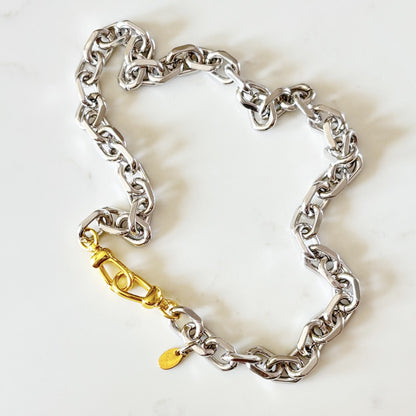 Riley chunky silver-toned chain bracelet with a 18K plated push clasp and a small gold tag, displayed on a light marble background.
