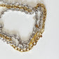 A close-up of three Rileyn interwoven chain necklaces, one silver-toned and one gold-toned, one Silver-tone with silver claps arranged on a light off-white background.