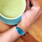 blue inclusiveness  Bracelet - Dress For Success Vancouver | Values Bracelet on wrist next to a blue cup with matcha