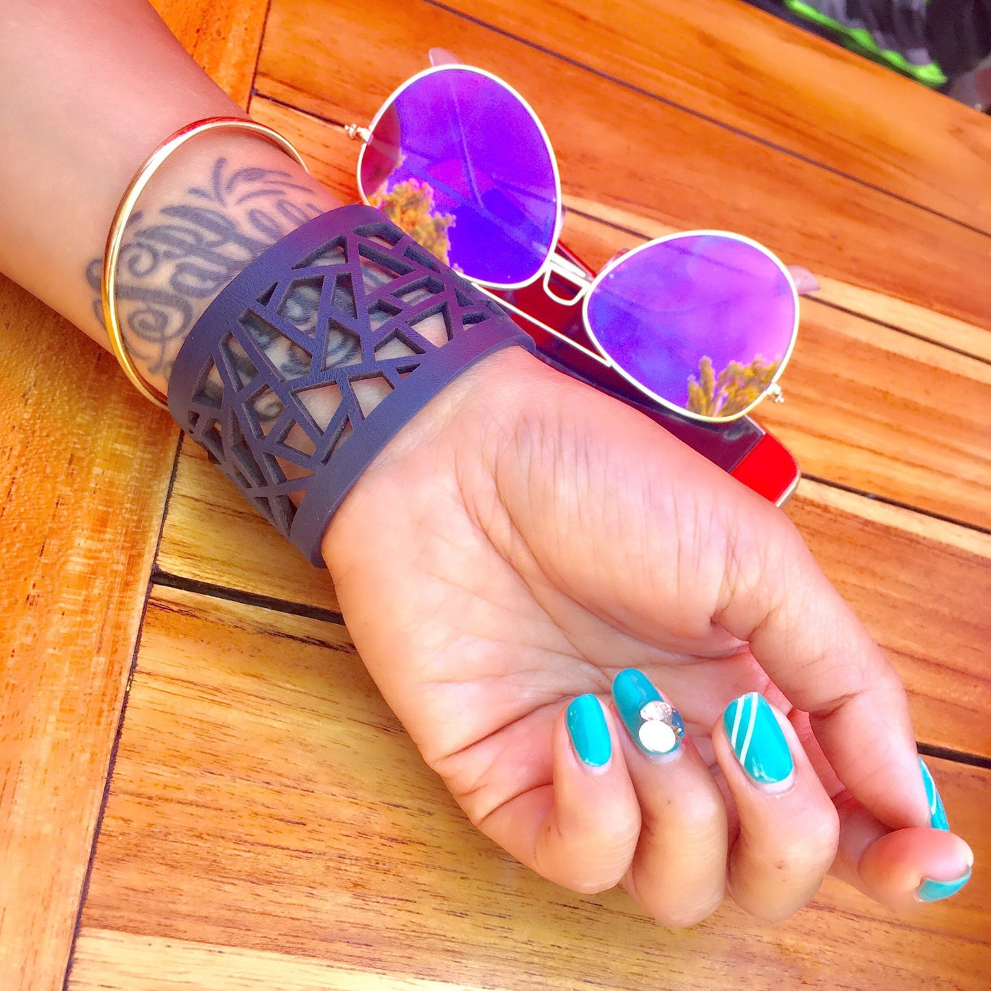 Blue manicured hand with tattoo against a table next to sunglasses wearing Margaret - Lattice Leather Laser Cut Bracelet
