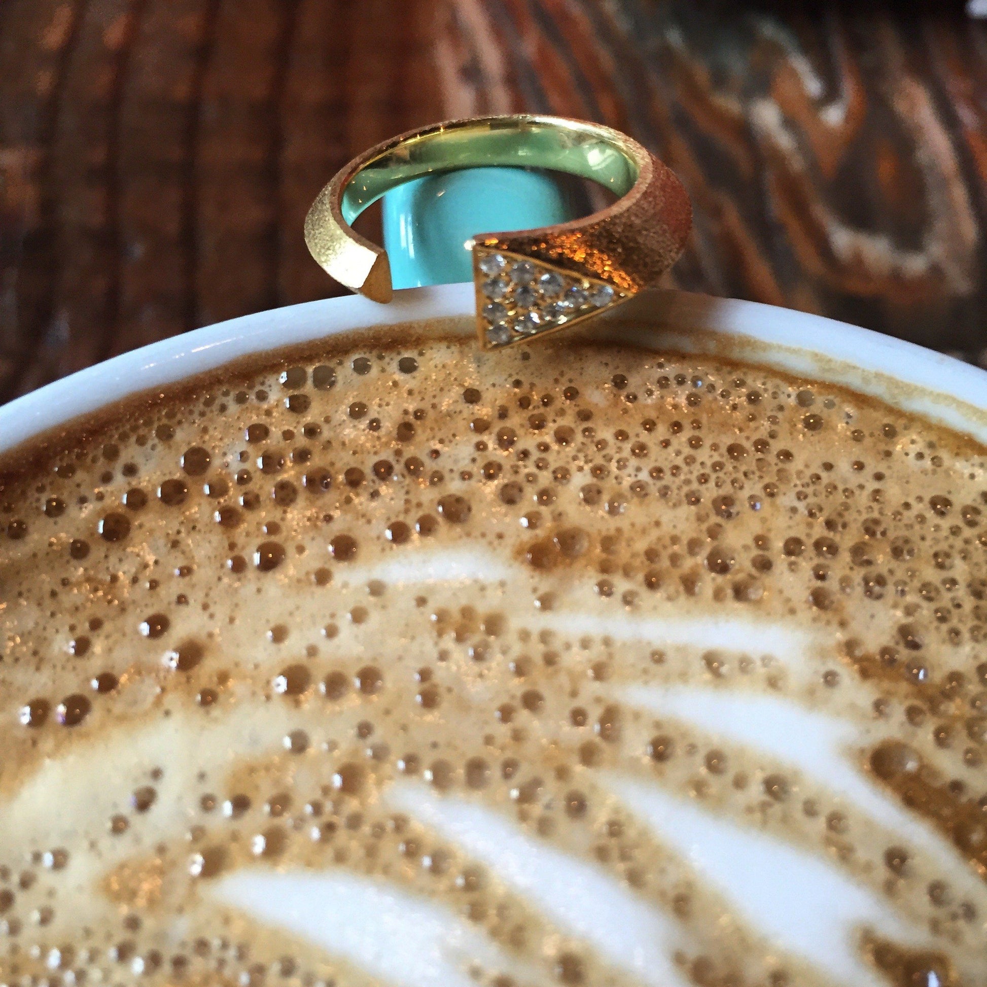 Mantra Dagger Open Ring With White Sapphires sitting on a turquoise cup with latte